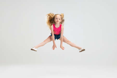 Beautiful little girl in casual clothes jumping isolated on white studio background. Happy childhood concept.の写真素材