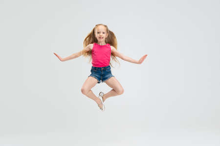 Beautiful little girl in casual clothes jumping isolated on white studio background. Happy childhood concept.の写真素材