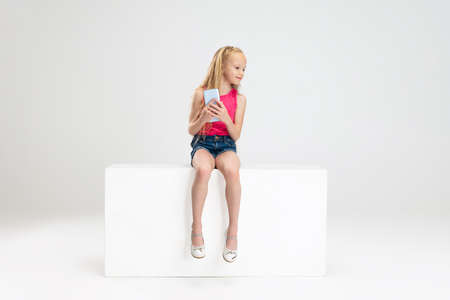 One beautiful little girl in casual clothes sitting on box isolated on white studio background. Happy childhood concept.の写真素材