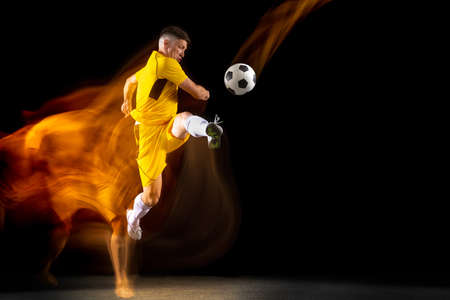 One caucasian male football or soccer player training with ball in mixed light isolated on dark background. Concept of professional sport, active, motion.の写真素材