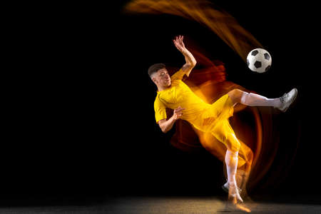 One caucasian male football or soccer player training with ball in mixed light isolated on dark background. Concept of professional sport, active, motion.の写真素材