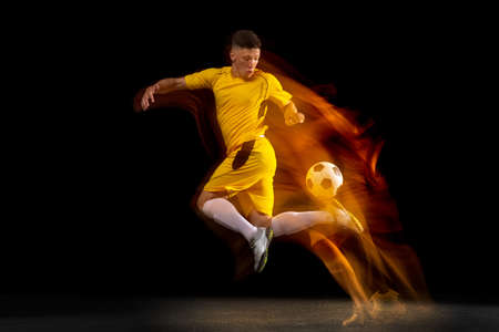 One caucasian male football or soccer player training with ball in mixed light isolated on dark background. Concept of professional sport, active, motion..の写真素材