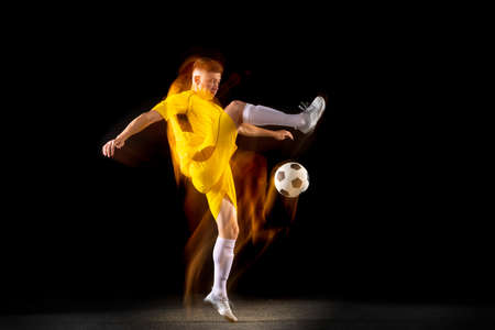 Young caucasian male football or soccer player kicking ball for the goal in mixed light on dark background. Concept of healthy lifestyle, professional sport, hobby.の写真素材