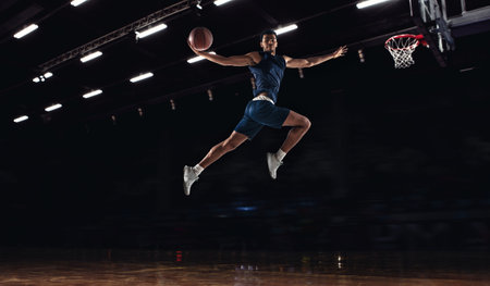 Young African sportsman, basketball player jumping high isolated on dark background. Concept of sport, game, competition. Dynamicの写真素材