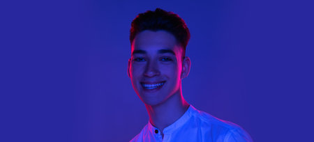 Close-up Caucasian young man posing isolated on blue studio background in neon pink light. Concept of human emotions, facial expression. Flyerの写真素材