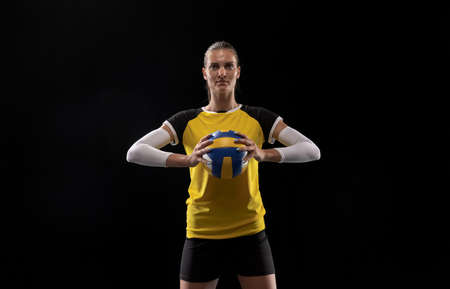 Young female volleyball player isolated on black studio background. Woman in sports equipment and shoes or sneakers training and practicing.の写真素材