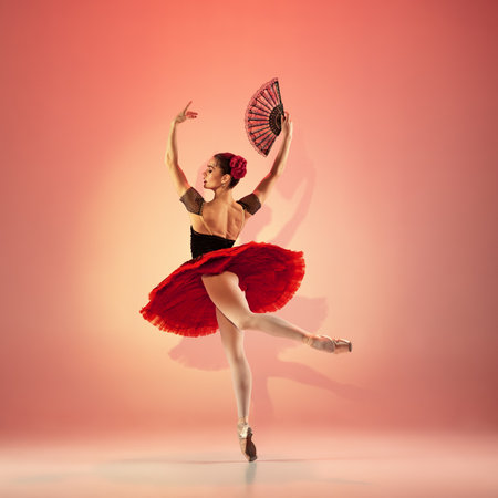 Young and incredibly beautiful ballerina is posing and dancing at red studio full of light.の写真素材