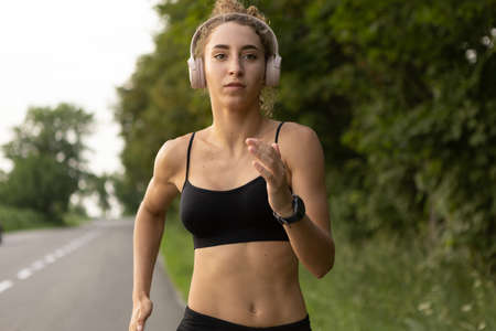 Young female runner, athlete is jogging at road in summer sunshine. Beautiful caucasian woman...
