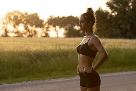 Young female runner, athlete is jogging at road in summer sunshine. Beautiful caucasian woman training, listening to music. Concept of sport, healthy lifestyle, movement, activity.の写真素材
