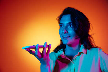 Recording voice message. Womans modern portrait on gradient orange studio background in neon.