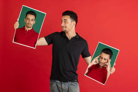 Young man holding his portraits isolated over red studio background with copyspace for ad.