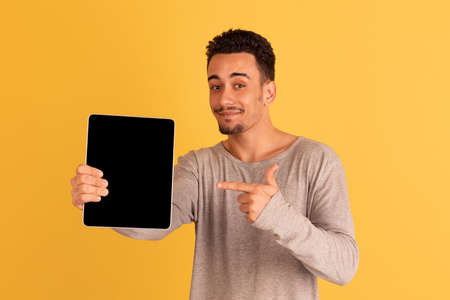 Pointing on tablet. Caucasian mans portrait isolated on yellow background with copyspace. Handsome...
