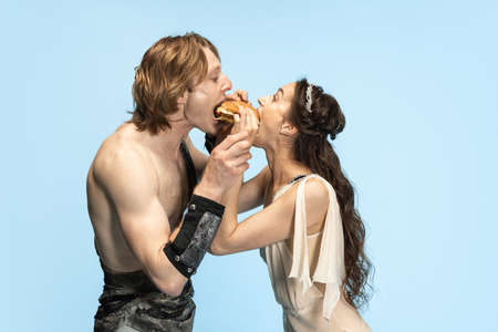 Burger and fast food. Young couple of ballet dancers in ancient Rome costums at blue studio.の写真素材