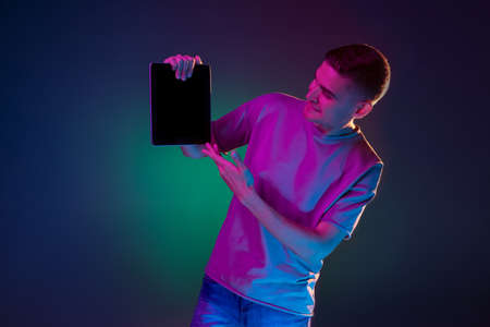 Young Caucasian man with digital tablet isolated over gradient blue green studio background in pink...