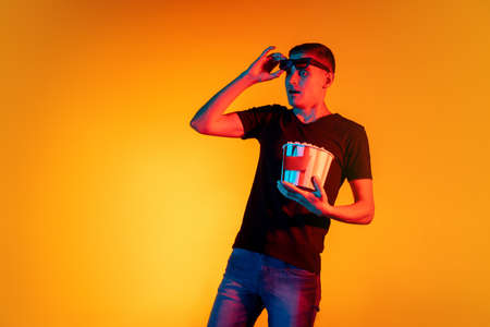 Portrait of young Caucasian man in casual clothes isolated over gradient red orange studio background in neon light with copyspace for ad. Concept of human emotionsの写真素材