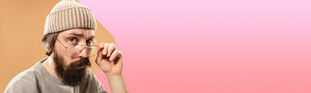 Young handsome man in glasses looking at camera isolated on gradient pink orange studio background.