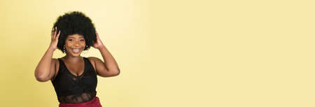 Portrait of African young woman isolated over light yellow studio background. Concept of human emotions, facial expression, youth, sales, ad.の写真素材