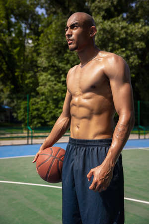Close-up young man, african male basketball player playing basketball at street public stadium, sport court or palyground outdoors. Summer sport games.の写真素材
