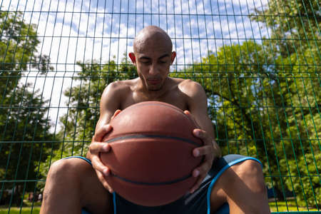 Close-up young man, african male basketball player playing basketball at street public stadium, sport court or palyground outdoors. Summer sport games.の写真素材