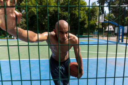 Young strong man, male basketball player practicing at street public stadium, sport court or...
