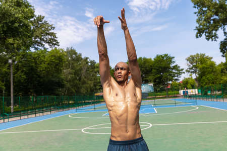 Strong muscular african-american male basketball player training at street public stadium, sport...