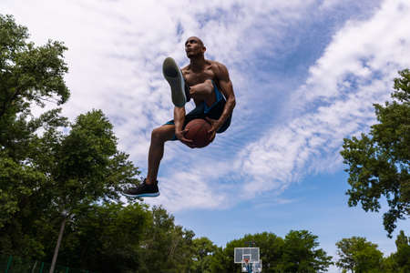 Young man, muscular african male basketball player playing basketball at street public stadium, sport court or palyground outdoors. Summer sport games.の写真素材