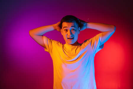 One Asian young man posing isolated on studio background in gradient pink purple neon light, colour filter. Concept of human emotions, facial expression.の写真素材