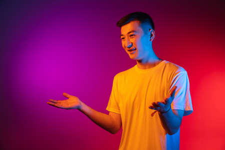 Portrait of Asian young man isolated on studio background in gradient pink purple neon light, colour filter. Concept of human emotions, facial expression.の写真素材