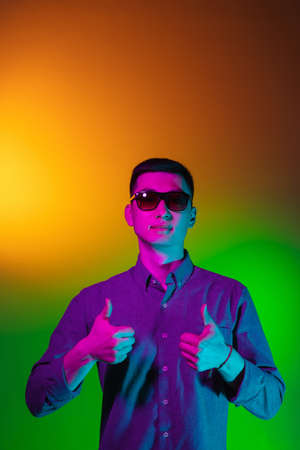 Portrait of Asian young man isolated on studio background in gradient green yellow neon light,...