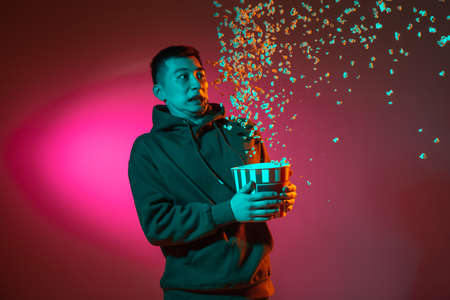 Half-length portrait of Asian young man isolated on studio background in gradient red neon light, colour filter. Concept of human emotions, facial expression.の写真素材