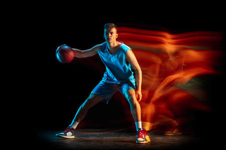 Young caucasian male basketball player playing basketball isolated over dark studio background in...