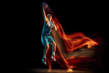 Young caucasian man, male basketball player playing basketball isolated over dark studio background in mixed light. Concept of healthy lifestyle, professional sport, hobby.の写真素材