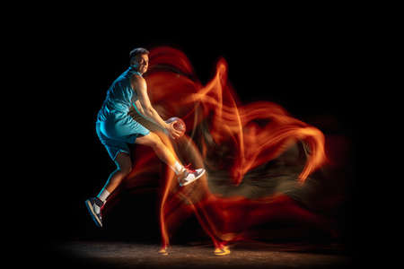 Young caucasian male basketball player playing basketball isolated over dark studio background in...