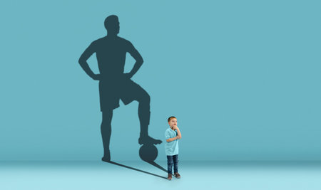 Childhood and dream about big and famous future. Conceptual image with boy and shadow of fit male football player on blue background. Dreams, imagination, education concept.の写真素材