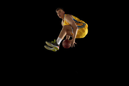 Jump shot. Basketball player with a ball in action and motion isolated on dark black studio...