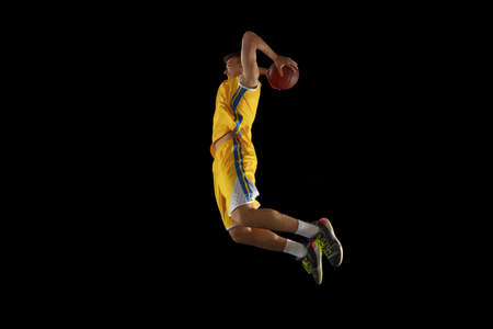 Young man, basketball player with a ball training isolated on dark black studio background. Advertising concept. Fit Caucasian athlete practicing with ball.の写真素材