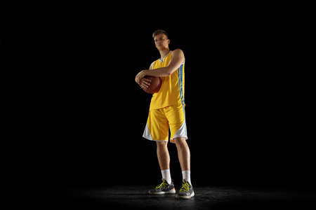 Portrait of young man, basketball player with a ball posing isolated on dark black studio background. Advertising concept. Before game, matchの写真素材