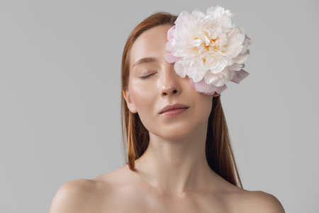 Close-up portrait of beautiful redheaded woman in lingerie with flower isolated over gray studio back ground. Fitness, diet, sports, natural beauty and aesthetic cosmetology concept.の写真素材