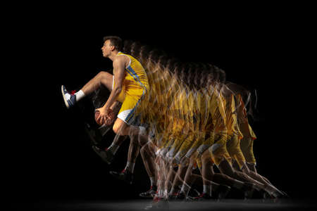 Portrait of young basketball player training with ball isolated on dark background with stroboscope...
