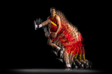 Portrait of young basketball player training with ball isolated on dark background with stroboscope effect. Concept of professional sport, hobby.の写真素材