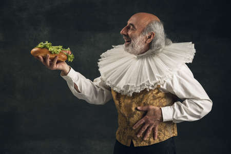 Elderly gray-haired man, medieval historical person, actor tasting fast foodの写真素材