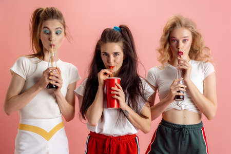 Pretty young women in retro 90s fashion style, outfits posing isolated over pink studio background. Concept of eras comparison, beauty, fashion and youth.の写真素材
