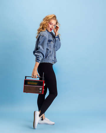 Portrait of pretty young girl in retro 90s fashion style, outfits posing isolated over blue studio...