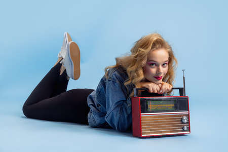 Portrait of attractive young girl in retro 90s fashion style, outfits posing isolated over blue studio background. Concept of eras comparison, beauty, fashion and youth.の写真素材