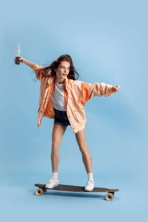 Beautiful adorable young girl in retro 90s fashion style, outfits on skateboard isolated over pink studio background. Concept of eras comparison, beauty, fashion and youth.の写真素材