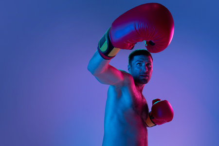 Close-up professional boxer in sportwear boxing on studio background in gradient neon light. Concept of sport, activity, movement, wellbeing.の写真素材