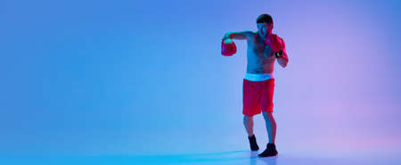 Caucasian man, professional boxer in sportwear boxing on studio background in gradient neon light. Concept of sport, activity, movement, wellbeing.の写真素材