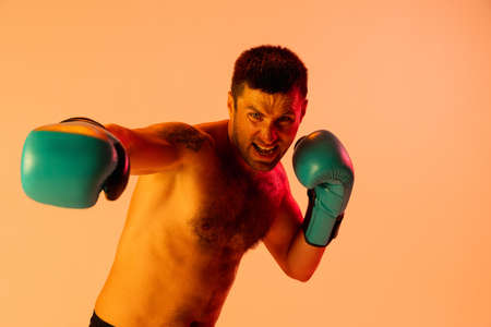 Close-up professional male boxer in sportswear and gloves isolated on yellow studio background in neon light. Concept of sport, activity, movement, wellbeing.の写真素材