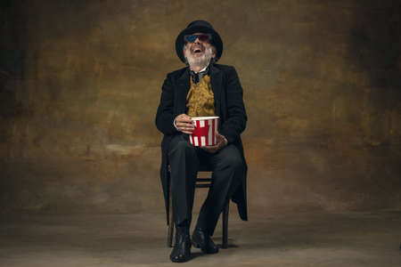 Cute senior smiling man, gentleman, aristocrat or actor watching movie isolated on dark vintage...
