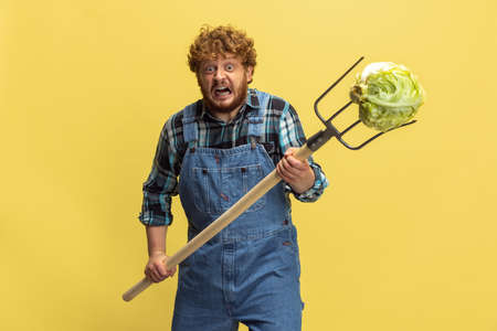 Portrait of young man, farmer with garden equipment isolated over yellow studio background. Concept...
